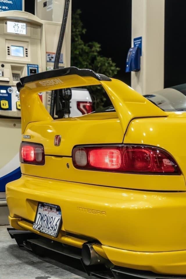 the back end of a yellow car at a gas station