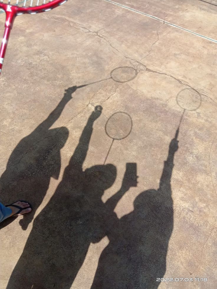 the shadow of two people holding tennis racquets