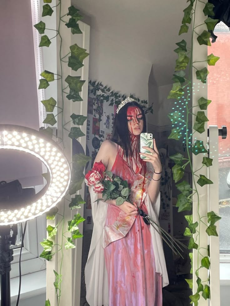 a woman dressed in costume taking a selfie with her cell phone while holding flowers