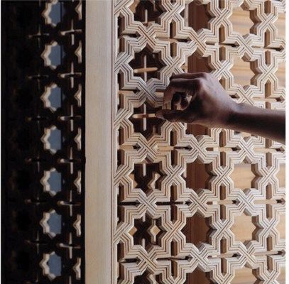 a hand that is holding something in front of a wall with geometric designs on it