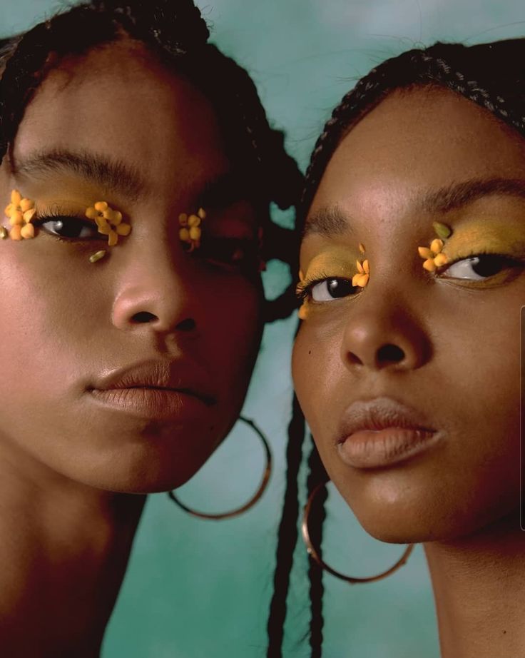 two young women with yellow flowers on their eyes are posing in front of a blue background