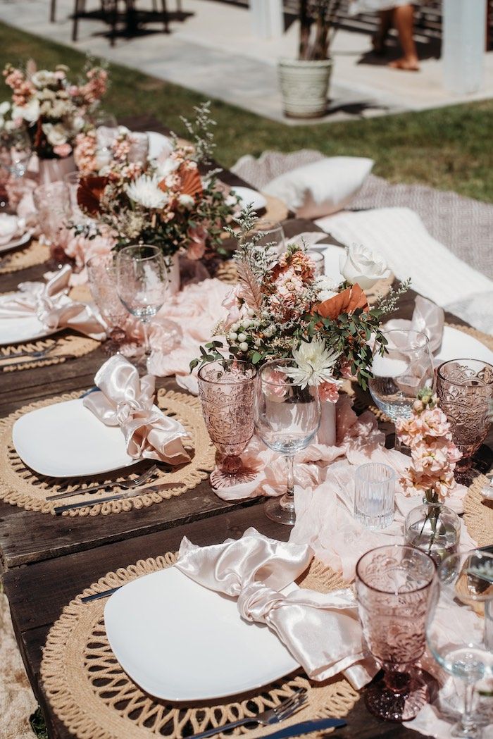 the table is set with pink and white flowers in glass vases, plates and napkins