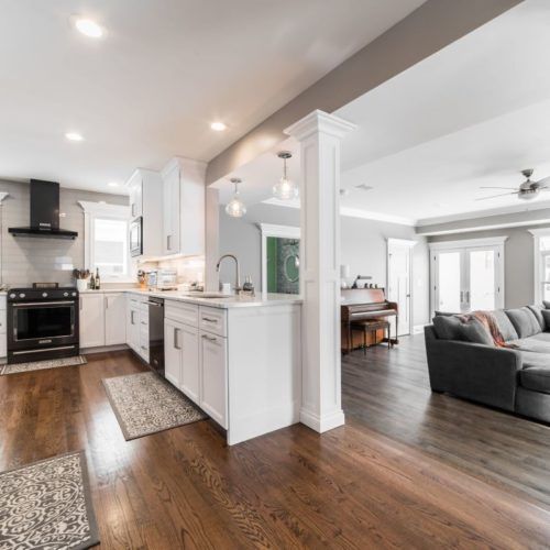 an open floor plan living room and kitchen area with hardwood floors, white cabinets, stainless steel appliances