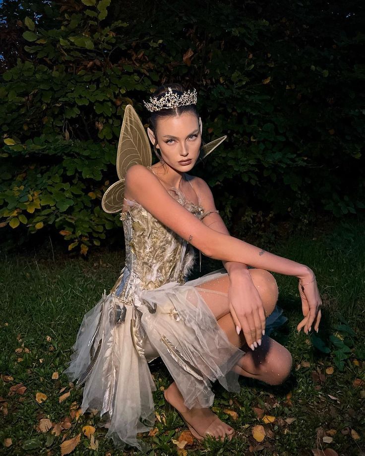 a woman dressed as tinkerbell sitting in the grass with her hands on her knees