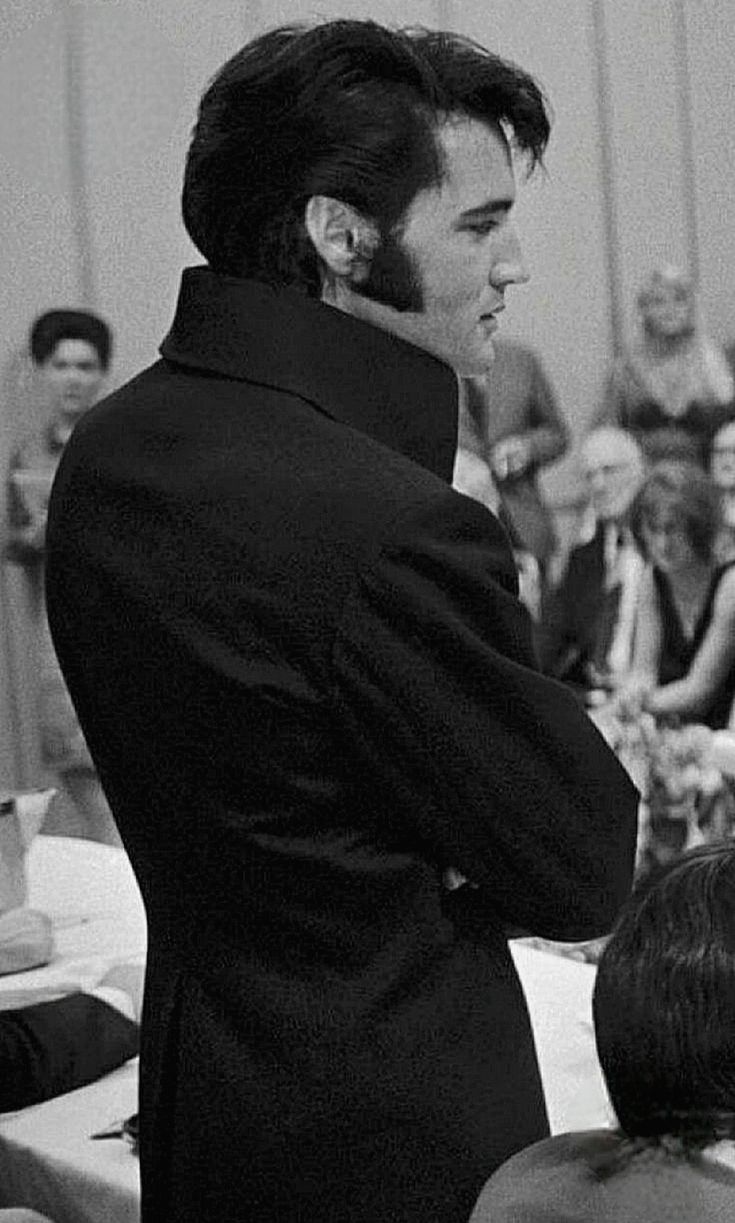 a black and white photo of a man in a tuxedo speaking to an audience