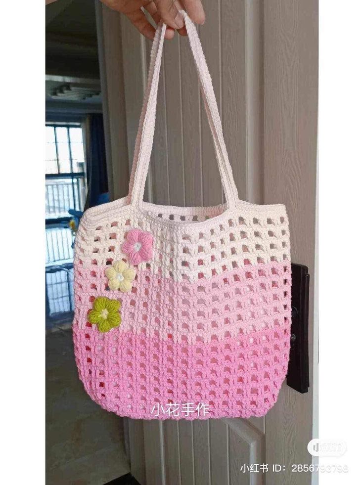 a hand holding a pink and white crocheted bag with flowers on it's handle