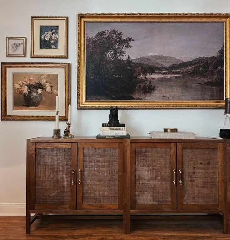 a painting hangs on the wall next to a sideboard with baskets and vases