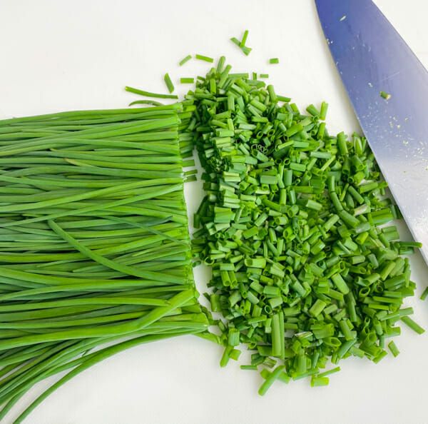 chopped up green onions next to a knife on a cutting board with the blades still attached