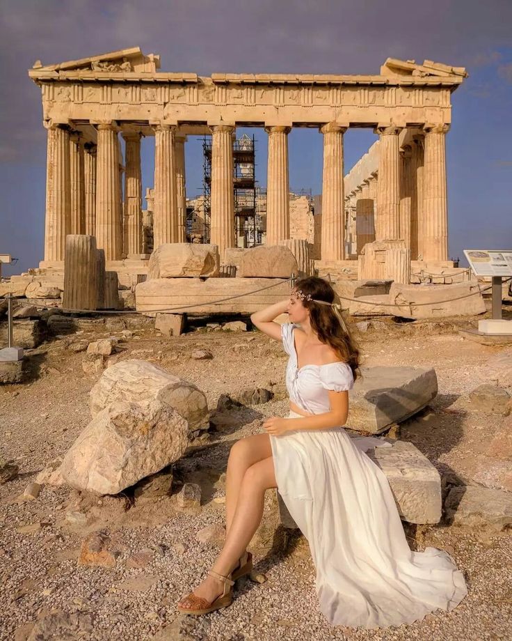 a woman sitting on top of a rock next to an ancient building in the background