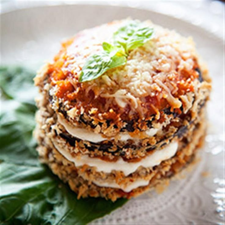 a stack of food on top of a white plate next to green leafy leaves