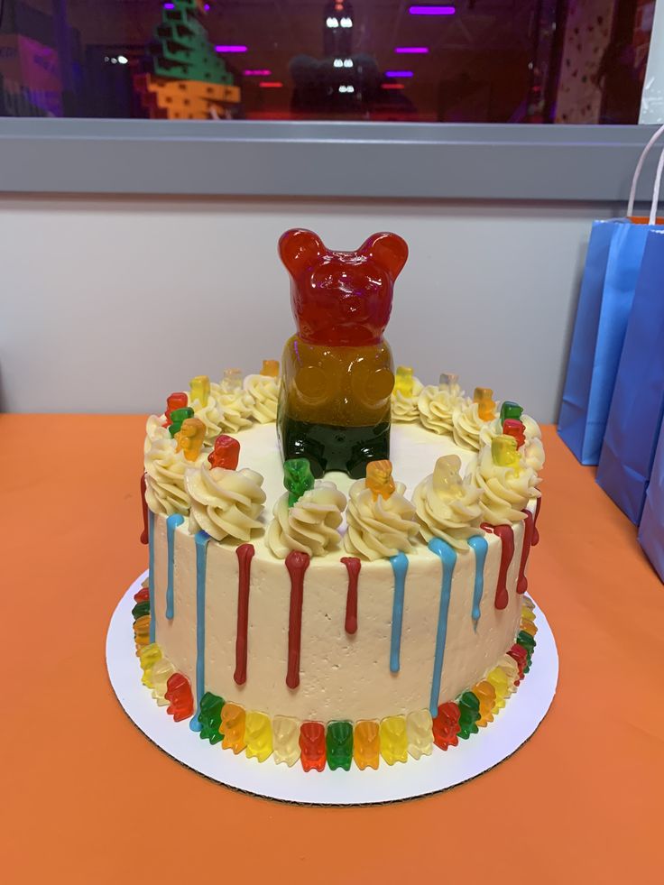 a birthday cake decorated with gummy bears and rainbow icing on an orange table