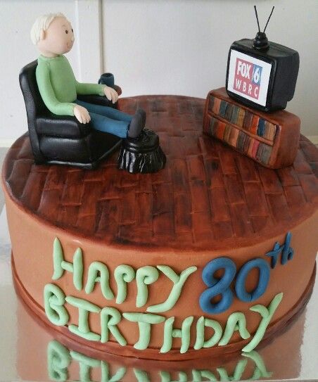 a birthday cake with a man sitting in a chair on top of the tv set