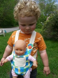 a toddler holding a baby doll in the grass