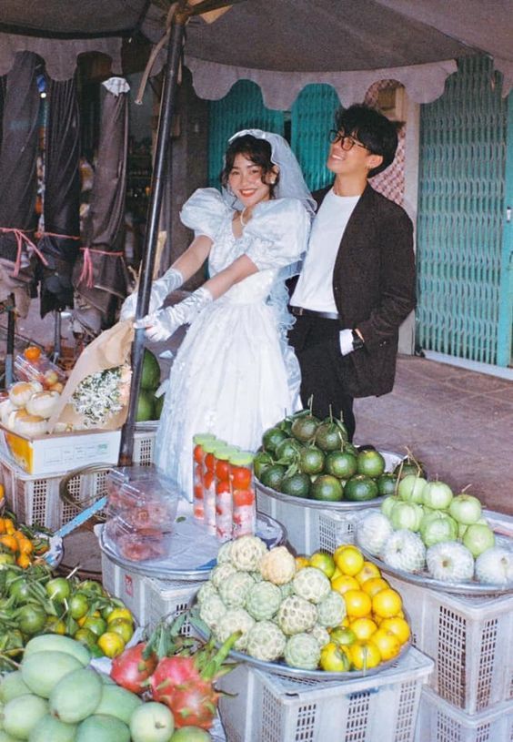 a man and woman standing next to each other in front of baskets filled with fruit