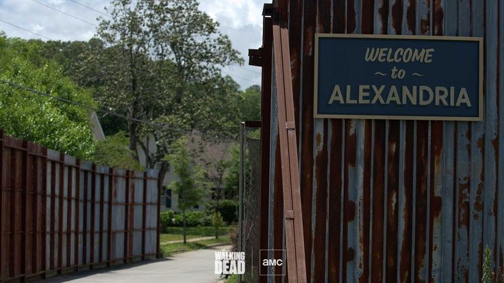 a welcome sign is posted on the side of a metal fence that has rusted wood slats