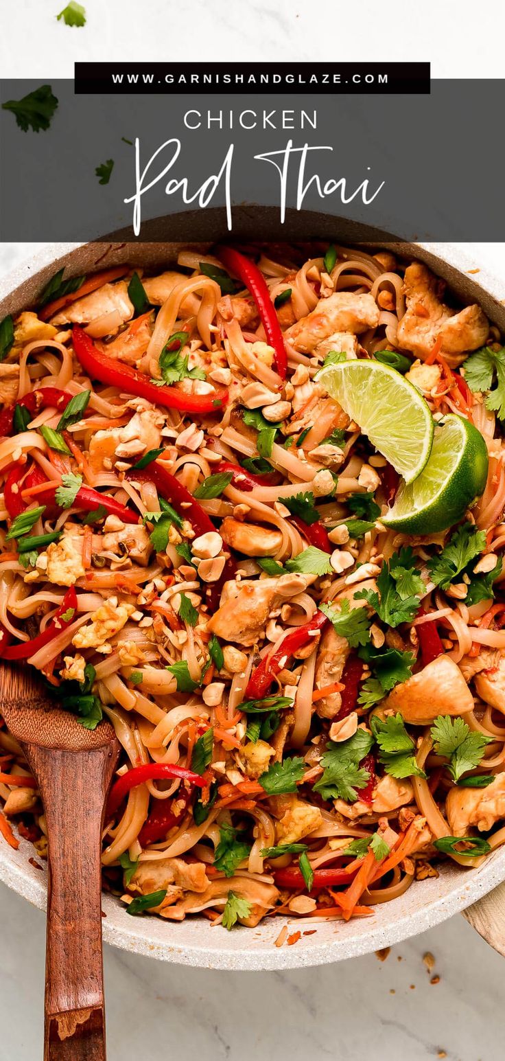 chicken pad thai noodles in a skillet with a wooden spoon and lime wedge on the side