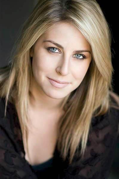 a woman with blonde hair and blue eyes posing for a photo in front of a black background