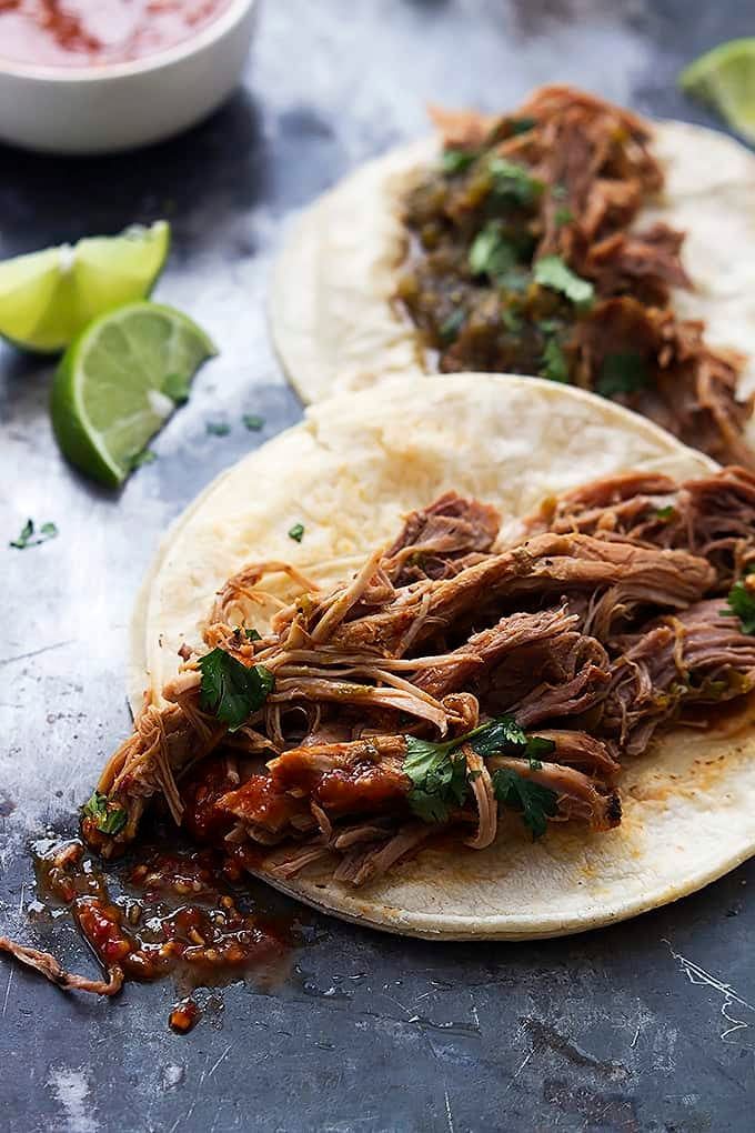 two pulled pork tacos on tortillas with salsa and limes next to it