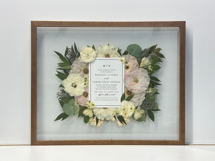 a frame with flowers and greenery in it