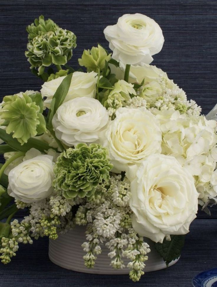 a bouquet of white flowers in a gray vase on a blue table cloth next to a plate