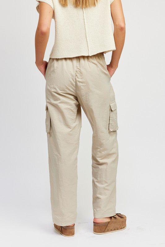 Cargo pants featuring a relaxed fit, side pockets and elastic around waist. The fun pants work for any season. Pair them with a sweater or a simple tee for an effortlessly chic look! Model is 5.9, wearing size S. Recommended sizing 2-4 S, 6 M, 8-10 L Elevated Casual Straight Cargo Pants With Elastic Waistband, Beige Parachute Pants With Elastic Waistband For Work, Elevated Casual Relaxed Pants With Elastic Waistband, Relaxed Pants With Elastic Waistband For Elevated Casual Occasions, Relaxed Pants With Elastic Waistband For Elevated Casual Wear, Versatile Bottoms With Side Pockets For Casual Wear, Versatile Bottoms With Side Pockets For Elevated Casual, Beige Cargo Pants With Elastic Waistband For Work, Relaxed Fall Bottoms With Pockets