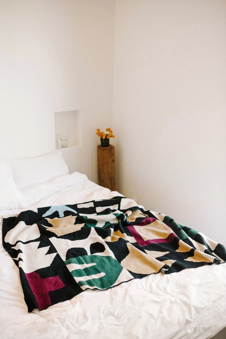 an unmade bed in a white room with flowers on the headboard and blanket