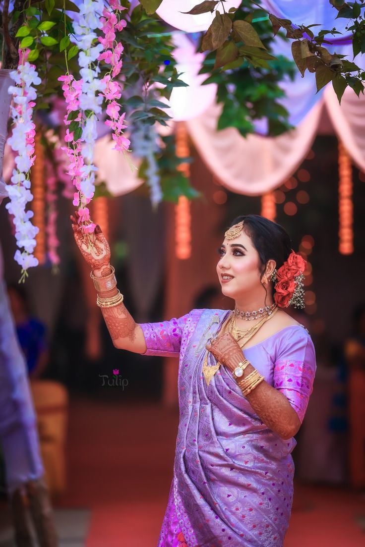 a woman in a purple sari holding flowers up to the sky with her hand