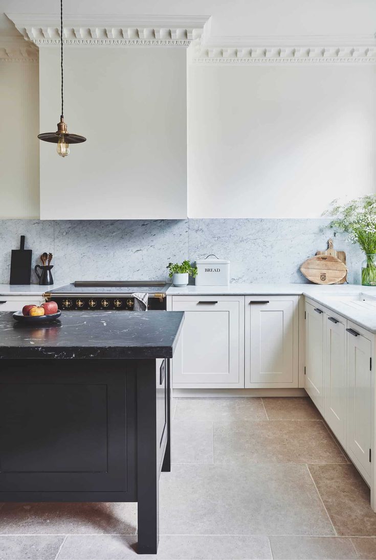 a kitchen with white cabinets and black counter tops, an island in the middle is surrounded by potted plants