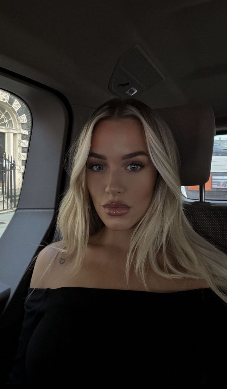 a woman with blonde hair sitting in the back seat of a car looking at the camera