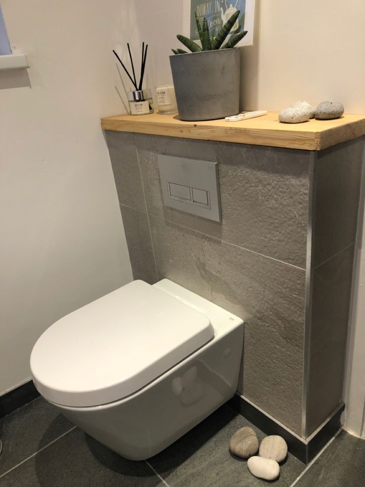 a white toilet sitting inside of a bathroom next to a wooden shelf with rocks on it