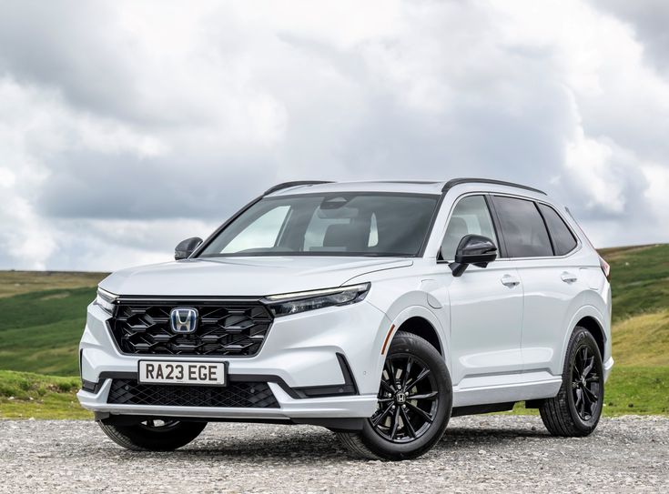 the front end of a white honda passport parked on top of a gravel road next to green hills