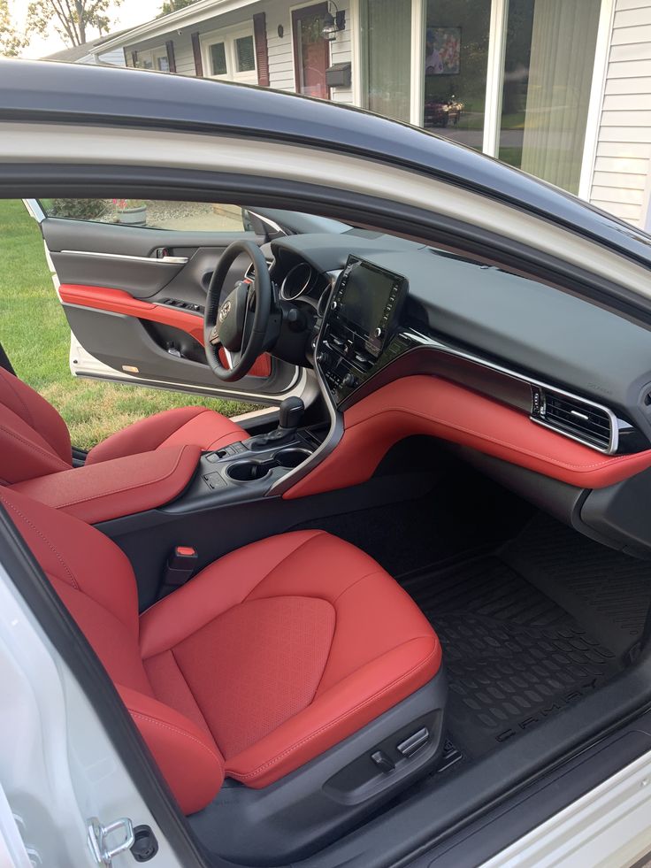 the interior of a car with red leather seats and dashboard, parked in front of a house