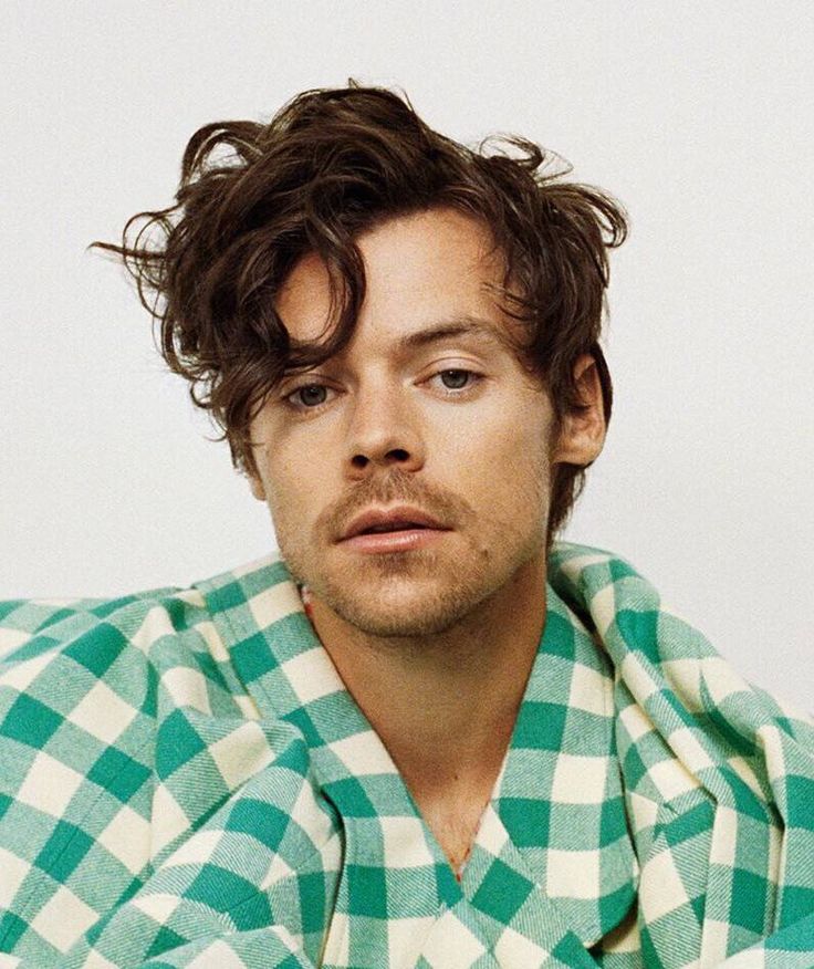 a man with curly hair wearing a green and white checkered shirt looking at the camera