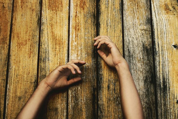 two hands reaching up against a wooden plank wall, with one hand on the floor