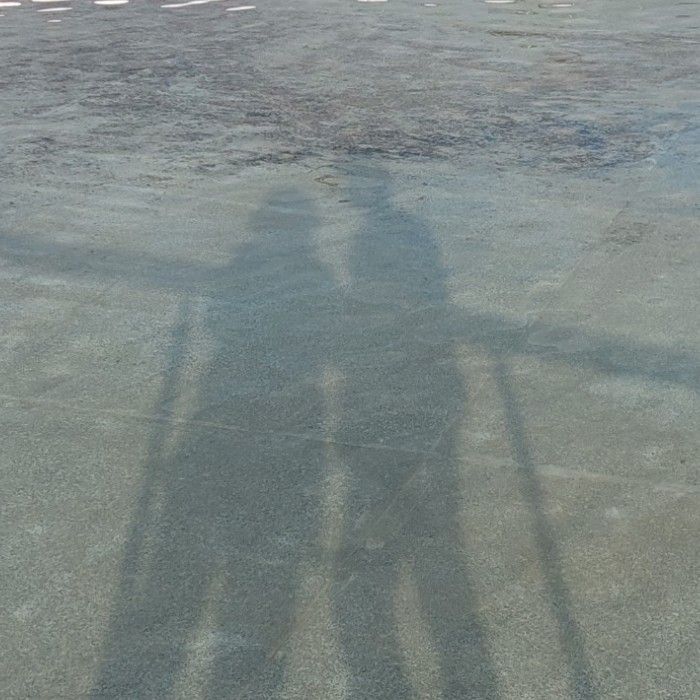 the shadow of a person holding a skateboard in front of an empty parking lot