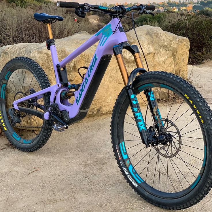 a purple and blue mountain bike parked next to a large rock