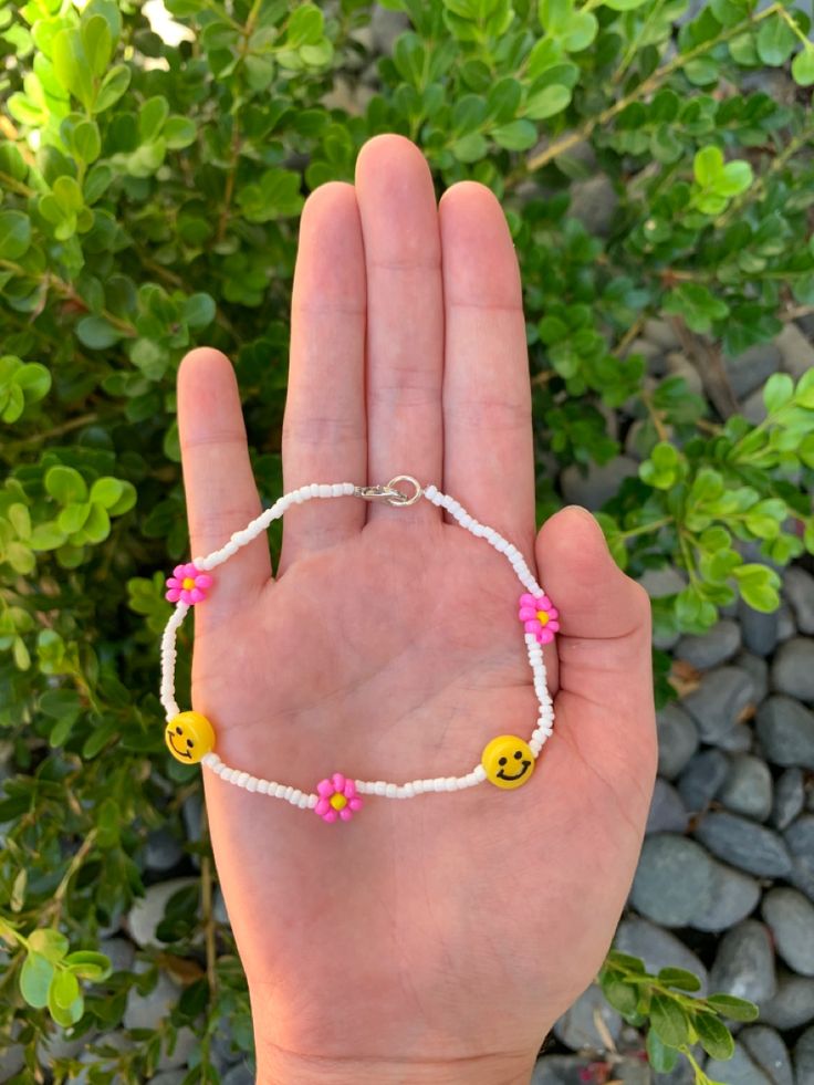 a hand holding a bracelet with smiley face beads and pink flowers on the bead