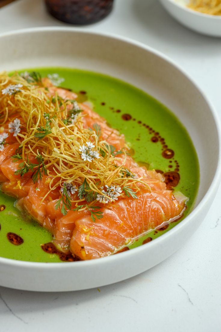 a white bowl filled with salmon covered in sauce and garnished with sprinkles