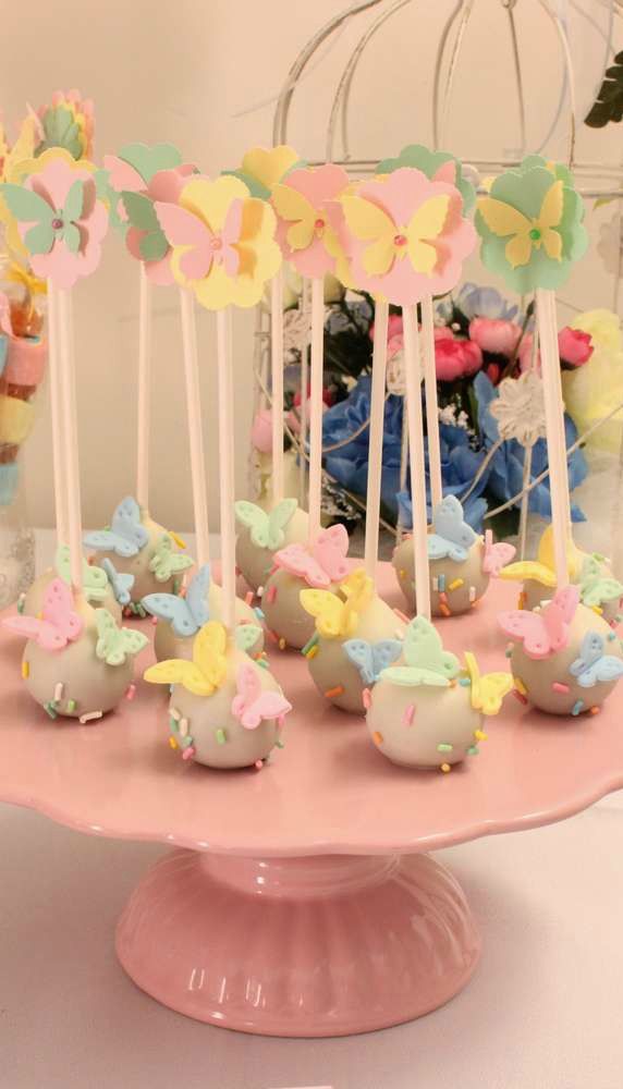 cake pops with butterflies on them sitting on a pink plate in front of other desserts