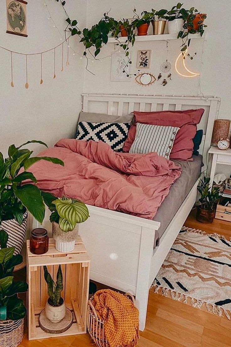 a white bed with pink sheets and pillows in a room filled with potted plants