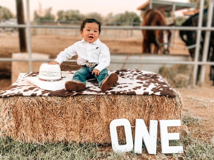 a young boy sitting on top of a hay bale with the word one painted on it