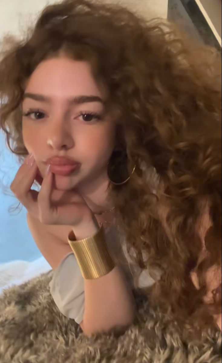 a woman with long curly hair laying on top of a fluffy rug wearing gold bracelets