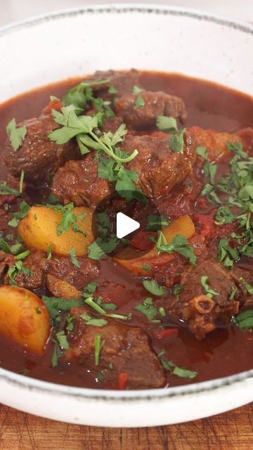 a bowl filled with meat and potatoes on top of a wooden table