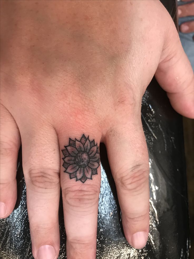 a person's hand with a small flower tattoo on the middle finger and bottom ring