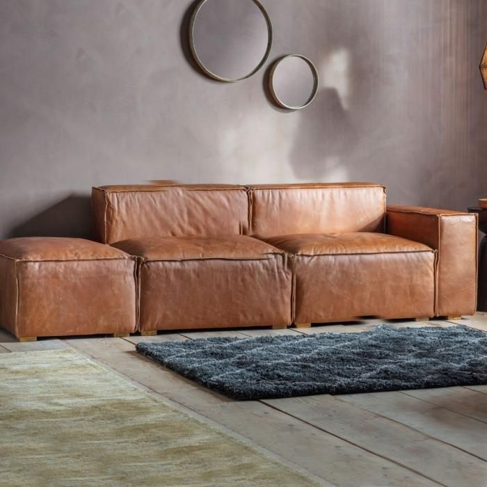 a brown leather couch sitting on top of a wooden floor next to a table and lamp