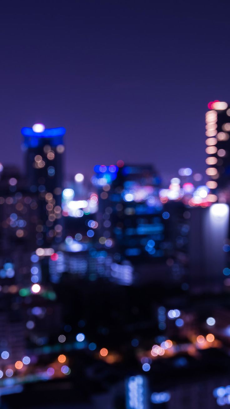 blurry cityscape at night with buildings and lights in the foreground, including skyscrapers