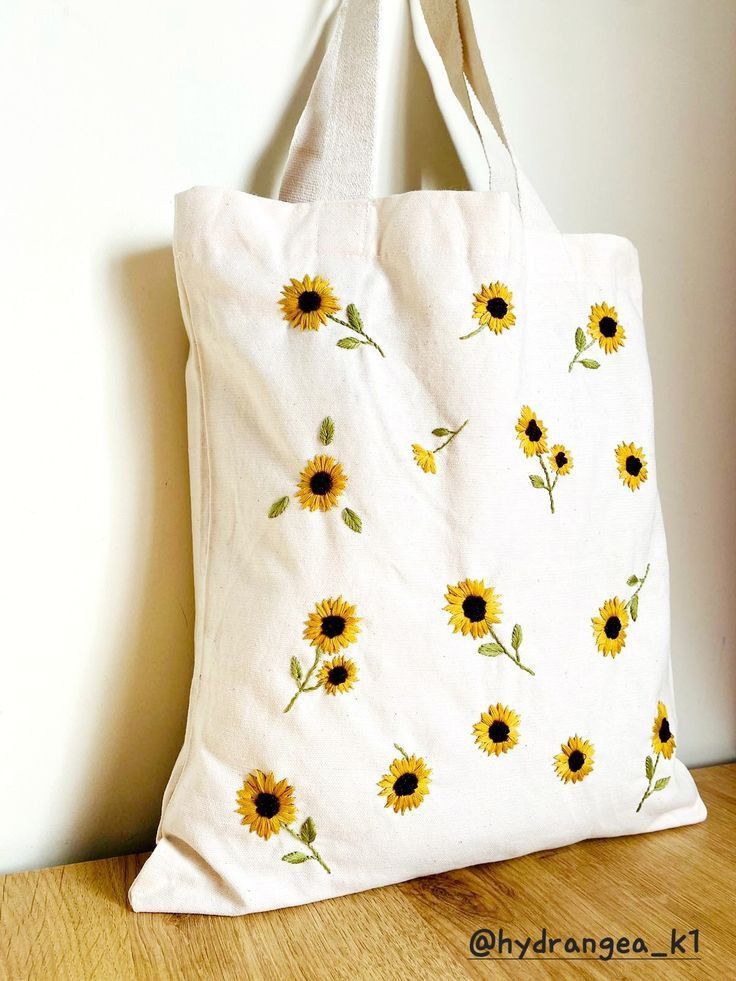 a white tote bag with sunflowers painted on it sitting on a wooden floor