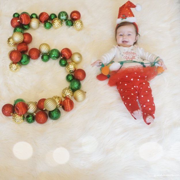 a baby laying next to christmas decorations on top of a white fur covered floor with the letter e spelled out