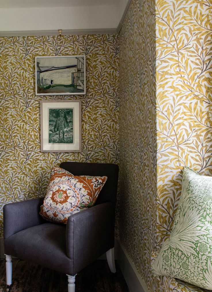 a chair in a room with wallpaper on the walls and pictures hanging above it