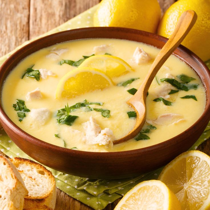 a wooden bowl filled with soup next to sliced lemons and bread on a table